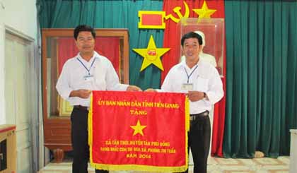 Chủ tịch UBND xã  Trương Hoàng Thanh (phải) và  Phó Chủ tịch  UBND xã Dương Thanh Tùng nhận Cờ thi đua của UBND tỉnh tặng xã Tân Thới.