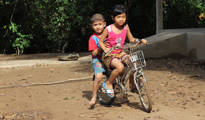 Không có khu vui chơi, em Nguyễn Thị Ngọc Trâm (8 tuổi, học sinh Trường Tiểu học thị trấn Mỹ Phước) dùng xe đạp chở em Nguyễn Lê Minh Trọng (5 tuổi) ở xã Tân Hòa Tây, huyện Tân Phước xung quanh sân nhà để vui chơi.