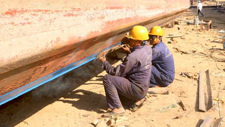 Công nhân hỗ trợ nhau ráp thanh thép vào thân tàu.