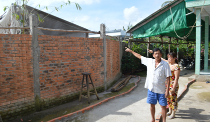 Anh Huỳnh Văn Tổng và chị Lê Thị Trang chỉ về trang trại heo được cách bởi bức tường.
