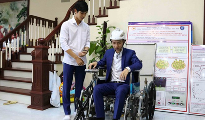Em Nguyễn Hữu Thành Đạt (bên trái) và Nguyễn Công Khánh thử nghiệm xe lăn leo cầu thang điều khiển bằng cử chỉ của đầu, giọng nói và điện thoại thông minh. (Ảnh: Thanh Thương/ TTXVN)