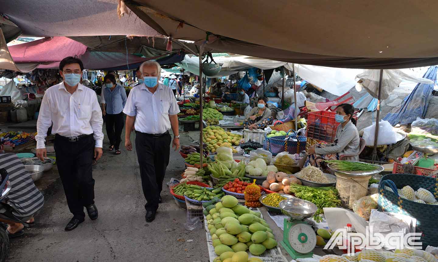 Đồng chí Nguyễn Văn Mười (bìa trái) kiểm tra việc đeo khẩu trang phòng chống dịch bệnh của người dân và các tiểu thương ở chợ Cái Bè.