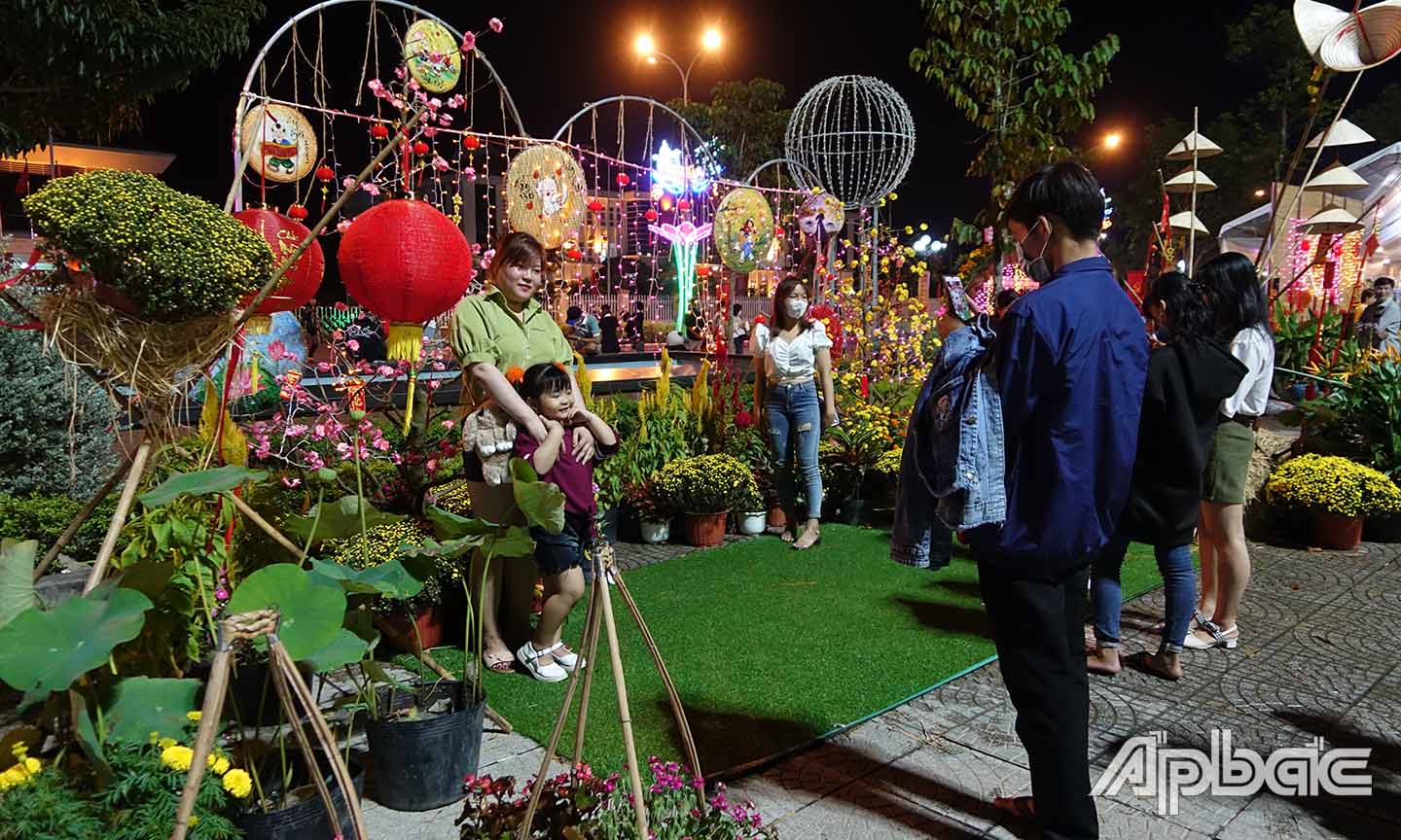 Người dân chụp ảnh lưu niệm tại cụm hoa xuân thị trấn Bình Phú, huyện Cai Lậy. Ảnh: QUẾ NGÂN