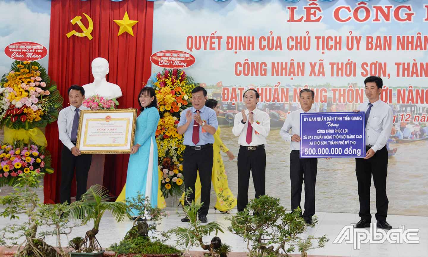 Đồng chí Nguyễn Ngọc Trầm (thứ 3 từ trái sang) và đồng chí Trần Kim Trát (thứ 3 từ phải sang) trao bằng công nhận xã NTM nâng cao và biểu trưng tặng công trình phúc lợi cho xã Thới Sơn.