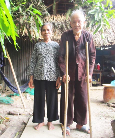 Ông Nguyễn Văn Ca đi đôi tó bằng cây  tầm vông cùng vợ trước căn nhà của mình.