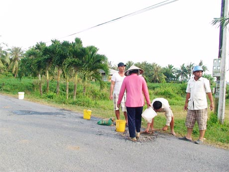 Ông Tư Thảm (đội nón bảo hiểm) cùng bà con ấp Long Bình san lấp “ổ gà” trên tuyến lộ 15.