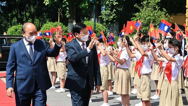  Vietnamese President Nguyen Xuan Phuc (L) and General Secretary of the Lao People’s Revolutionary Party Central Committee and President of Laos Thongloun Sisoulith wave hands at children at the welcome ceremony in Hanoi on June 28. (Photo: VNA).