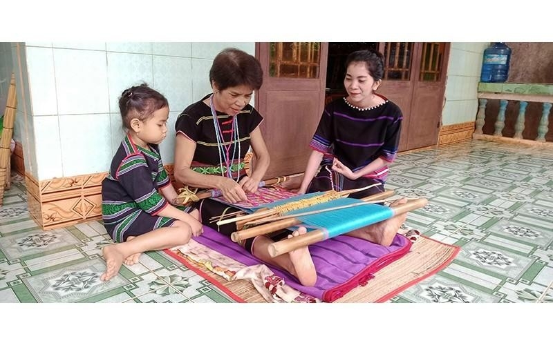 Artisan Thi An De (Tho Son Commune, Bu Dang District, Binh Phuoc Province) transfers her knowledge of traditional brocade weaving to her descendants. (Photo: NHAT SON).