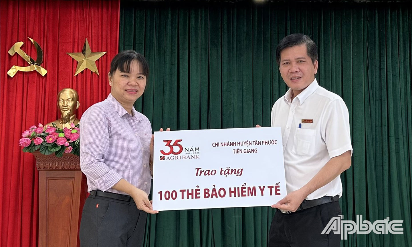 Ông Nguyễn Thành Thắng, Phó giám đốc Agribank huyện Tân Phước trao biển tượng trưng 100 thẻ bảo hiểm y tế cho bà Đặng Thị Ngọc Hiền, Phó Giám đốc Bảo hiểm Xã hội huyện Tân Phước.