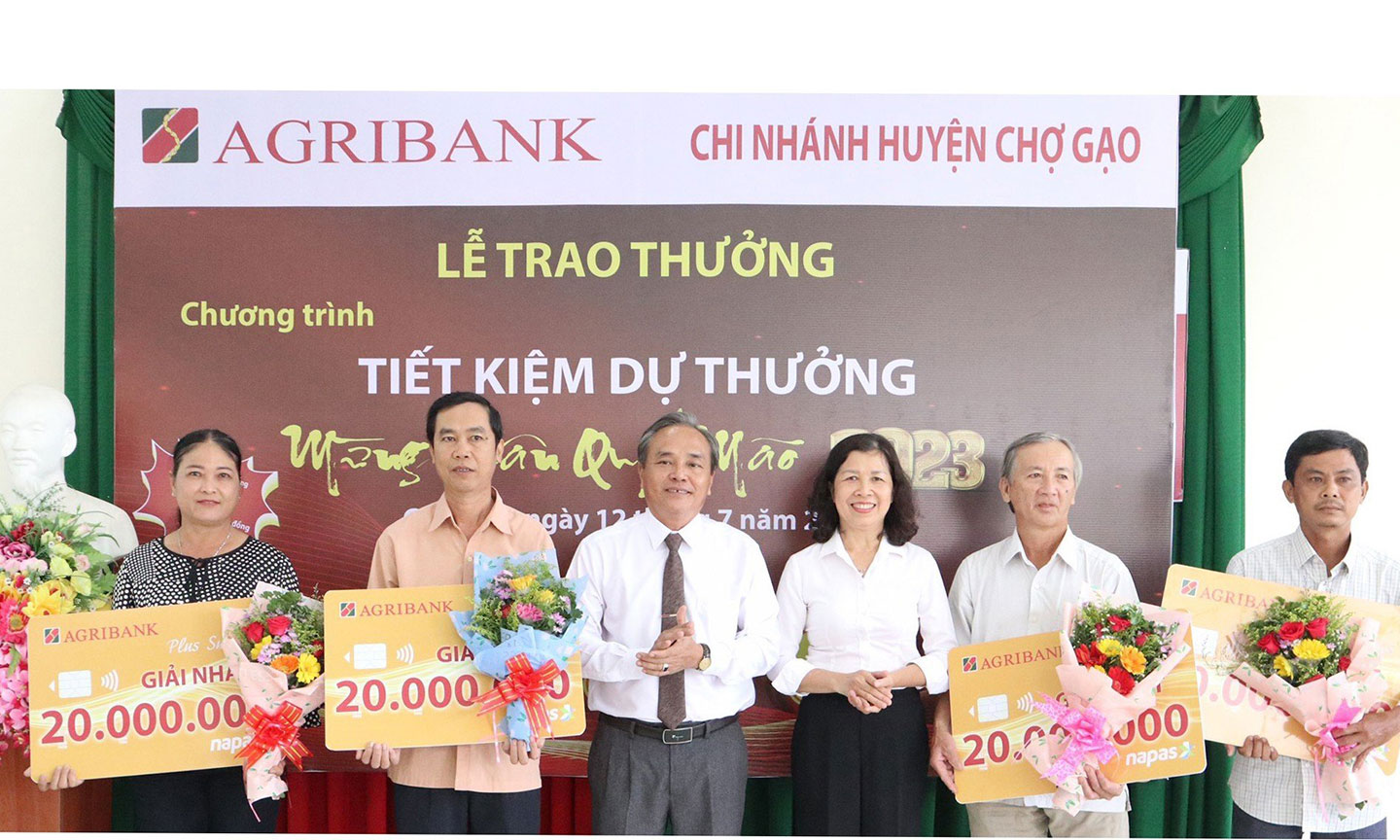 Bà Nguyễn Ngọc Oanh, Phó Giám đốc Agribank Tiền Giang trao thưởng cho khách hàng của Agribank Chợ Gạo trúng thưởng giải Nhất và ông Cao Tấn Hưởng, Ủy viên Ban Thường vụ Huyện ủy, Phó Chủ tịch UBND huyện Chợ Gạo tặng hoa chúc mừng.