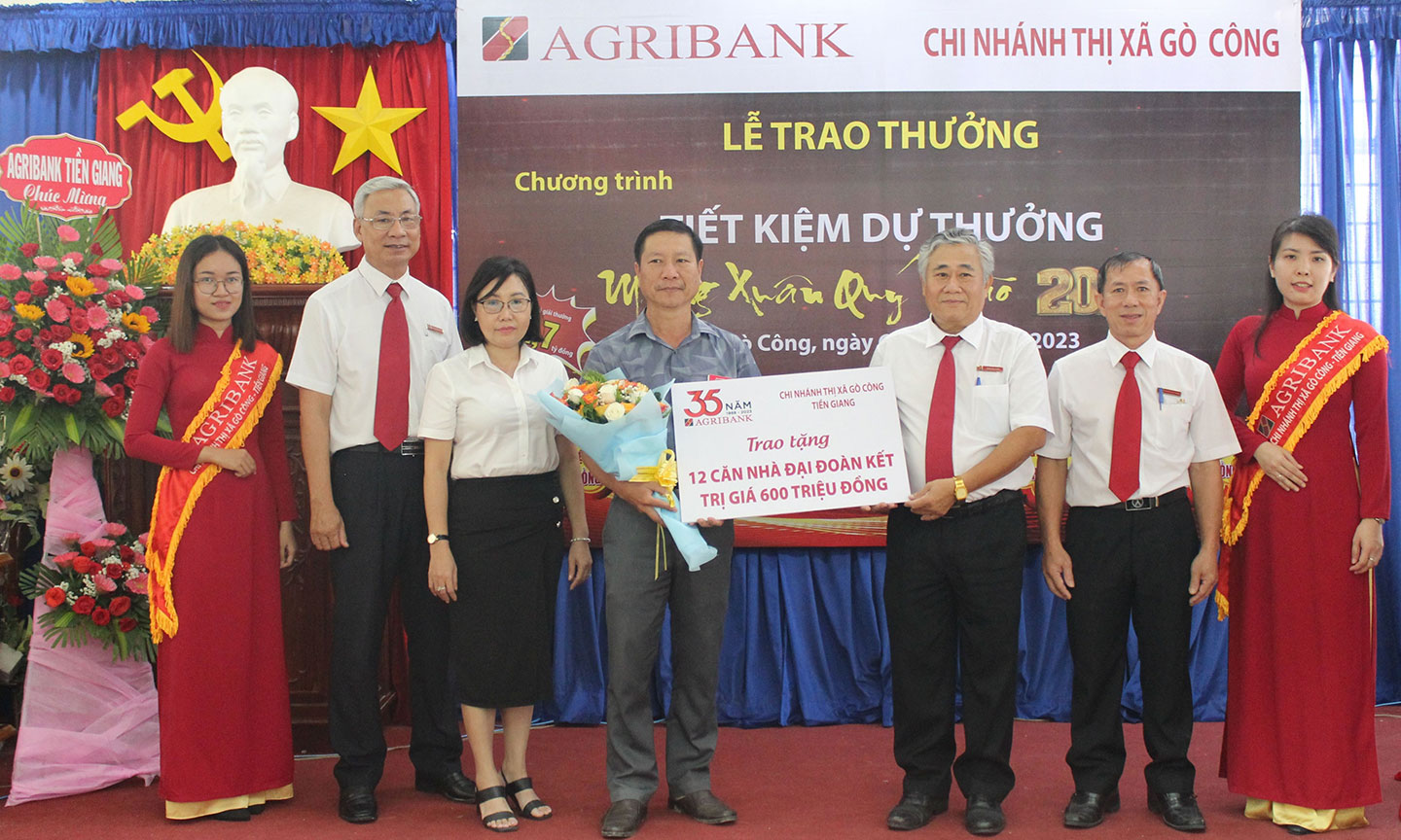 Ông Trần Phi Châu, Giám đốc Agribank TX. Gò Công  trao biển tượng trưng số tiền 600 triệu đồng xây tặng 12 căn nhà đại đoàn kết cho ông Phạm Thanh Nguyên, Ủy viên Ban Thường vụ, Trưởng Ban Dân vận, Chủ tịch UBMTTQ TX. Gò Công –trước sự chứng kiến của bà Đinh Thị Thanh Tuyền, Phó Giám đốc Agribank Tiền Giang (thứ hai từ trái) và Ban Giám đốc Agribank TX. Gò Công