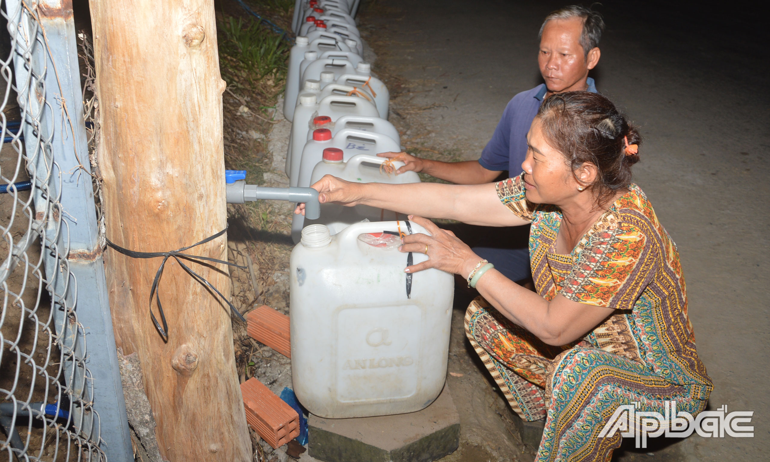 Bà Võ Thị Nhỉ (ấp 3, xã Gia Thuận) canh lấy nước sinh hoạt tại vòi công cộng trước nhà cho những hộ dân xung quanh. Dù đã hơn 19 giờ đêm, nhưng vẫn không có nước. 