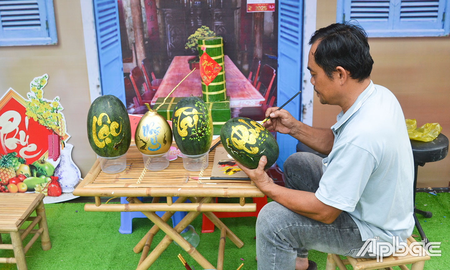 Anh Nguyễn Văn Sang  đang viết chữ thư pháp và  kết hợp với vẽ các họa tiết lên sản phẩm  trái dưa hấu. 